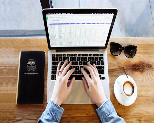 Hands typing on a laptop keyboard near a cup of coffee